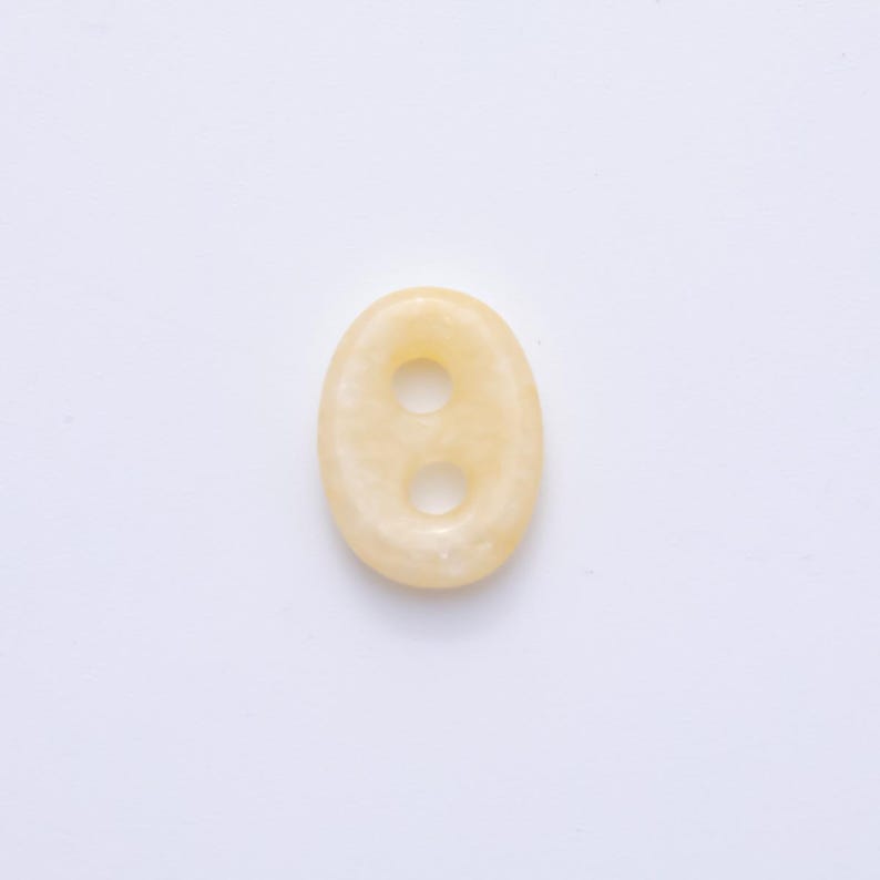 May include: Oval-shaped, pale yellow button with two holes. The button has a smooth, polished surface and a slightly translucent appearance. The button is set against a white background.