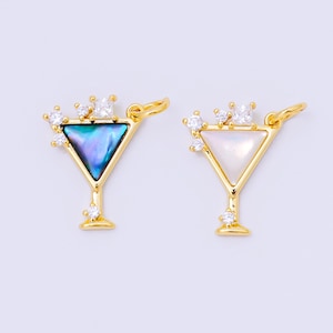 May include: Two gold-colored martini charm pendants. One features a triangular abalone shell inlay, the other a white mother-of-pearl inlay. Both charms are adorned with small, clear crystals and a square crystal at the top.