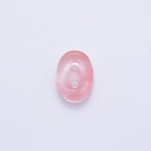 May include: Oval-shaped, translucent pink button with two holes. The button has a subtle, marbled appearance, with variations in the pink hue. The button is a sewing or craft supply.