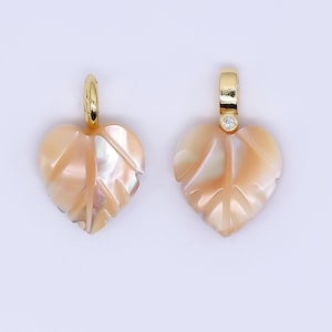 Peut inclure: Deux pendentifs en forme de feuille. Chaque pendentif est de couleur pêche clair avec des reflets irisés et une bélière dorée. Un pendentif a une petite pierre précieuse transparente sertie dans la bélière.