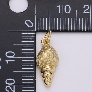 May include: Gold-coloured seashell charm pendant. The seashell is detailed with a textured surface and a spiral design. The charm is approximately 2.5 cm in length.