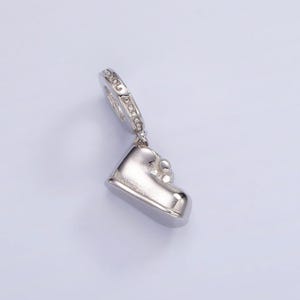 May include: Silver charm in the shape of a shoe with a small circle of clear stones at the top.