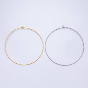 May include: Two metal hoop earrings, one gold-toned and one silver-toned, are displayed against a white background. The hoops are circular and have a simple, minimalist design. The earrings are likely for ear piercing.