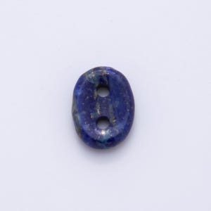 May include: Oval-shaped lapis lazuli button with two holes. The button is a deep blue color with flecks of gold throughout. The button is set against a white background.