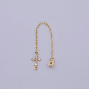 May include: Gold chain extender with a small, clear crystal cross charm and a lock charm. The extender is about 2 inches long.