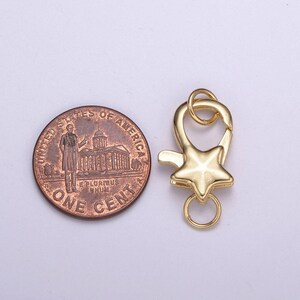 May include: Gold-toned metal star-shaped clasp with a ring for attaching to a necklace or bracelet. The clasp is shown next to a US penny for size comparison.