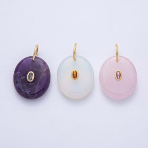 May include: Three gemstone pendants with gold-colored bails. The pendants are oval-shaped, with one in amethyst, one in white, and one in pink. Each pendant has a small, oval-shaped gemstone in the center. The pendants are displayed against a white background.