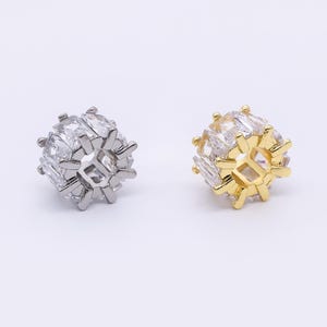 Peut inclure: Deux perles décoratives en forme d'anneau. L'une est argentée, l'autre dorée. Les deux présentent des pierres précieuses claires, de coupe rectangulaire, serties sur le bord extérieur. Les perles ont un centre creux et ouvert.