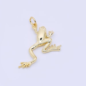 May include: A gold-colored frog pendant with a jump ring for attaching to a necklace or bracelet. The frog is in a dynamic pose, with its legs bent and arms raised. The pendant has a smooth, polished finish.