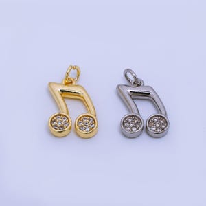 May include: Two musical note pendants. One is gold-colored, the other is silver-colored. Each pendant has two round, gem-studded accents. The pendants are designed to be used as jewelry.