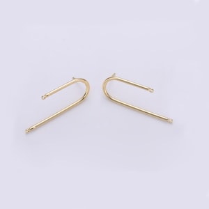 May include: A pair of gold-colored, minimalist earrings. Each earring has a curved, U-shaped design with a small ball at each end. The earrings are presented on a light background, highlighting their simple elegance.