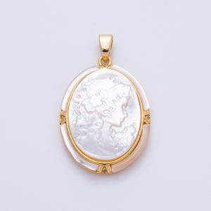 May include: Oval pendant with a cameo of a woman's profile carved in white, set in a gold-tone frame. The pendant has a bail at the top for a chain. The cameo features intricate details of the woman's hair and clothing.