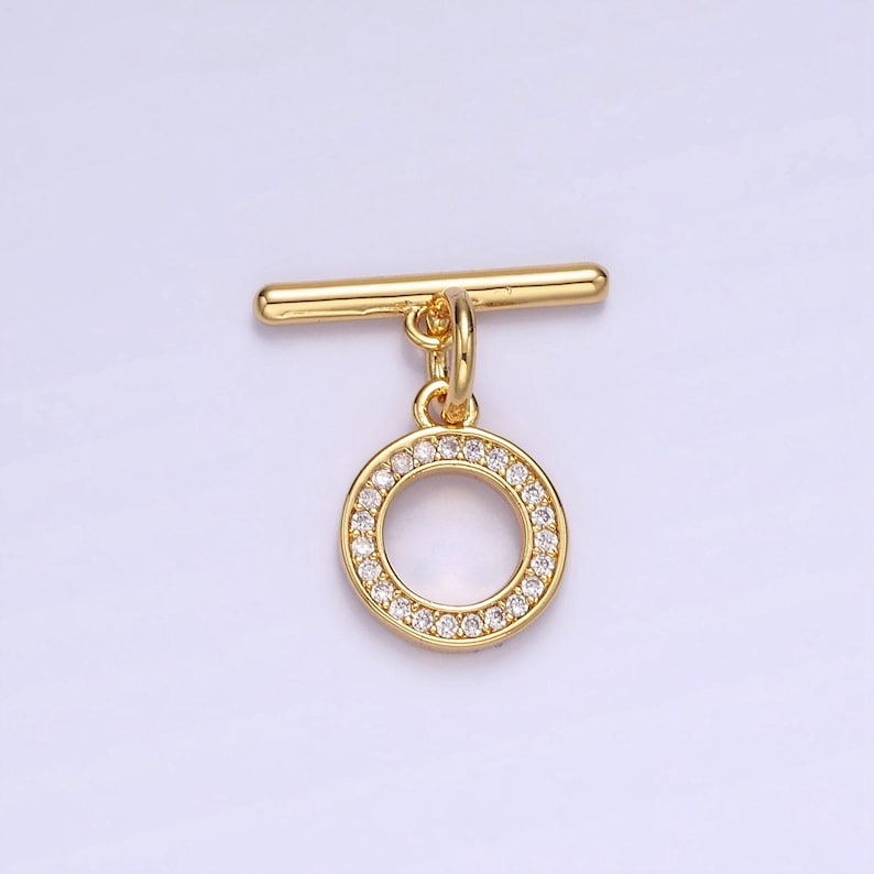 Pode incluir: Fecho de correr dourado com um pingente redondo incrustado com strass transparentes.