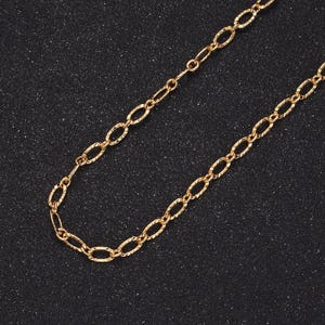 May include: A gold-colored necklace with an oval link chain design. The chain has a textured surface and is displayed against a dark background. The necklace is a jewelry item.
