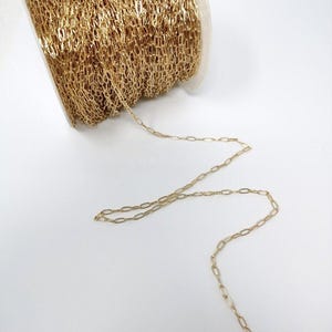 May include: A spool of gold-colored chain, with a portion of the chain uncoiled and hanging down. The chain is made of small, oval-shaped links.
