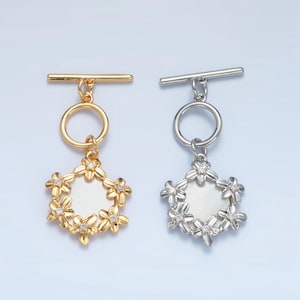 May include: Two toggle clasps with a floral design. The clasp on the left is gold with a white background and the clasp on the right is silver with a white background.