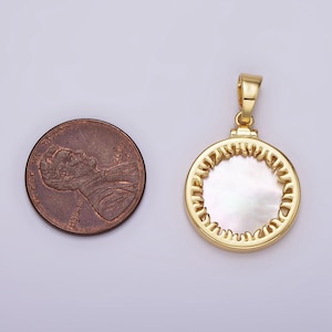 Puede incluir: Un colgante de oro con una incrustación redonda de nácar blanco. El colgante está rodeado por un borde dorado decorativo.