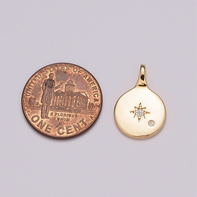 May include: Gold pendant featuring a small diamond star and a single diamond. The pendant is approximately the size of a UK penny.