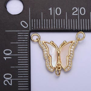 May include: Gold-tone butterfly charm with clear rhinestones and a white mother-of-pearl inlay. The charm has two jump rings for attaching to a necklace or bracelet.