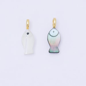 Puede incluir: Dos colgantes con forma de pez. Uno es blanco con un ojo de punto negro, el otro es iridiscente con un contorno negro. Ambos tienen aros dorados en la parte superior para colgar. Los colgantes son probablemente dijes de joyería o aretes.