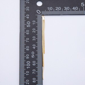 May include: A gold-colored, multi-strand chain, likely for jewelry, hangs vertically against a black ruler. The ruler displays centimeter measurements. The chain's delicate strands are visible, suggesting a lightweight design. The background is a plain white surface.