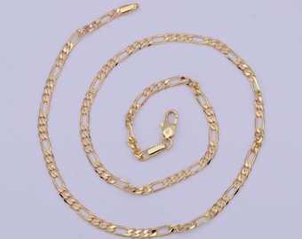 May include: A gold-colored Figaro chain necklace. The necklace features a pattern of three small circular links followed by one elongated oval link. The chain is displayed on a light purple background and has a lobster clasp closure.