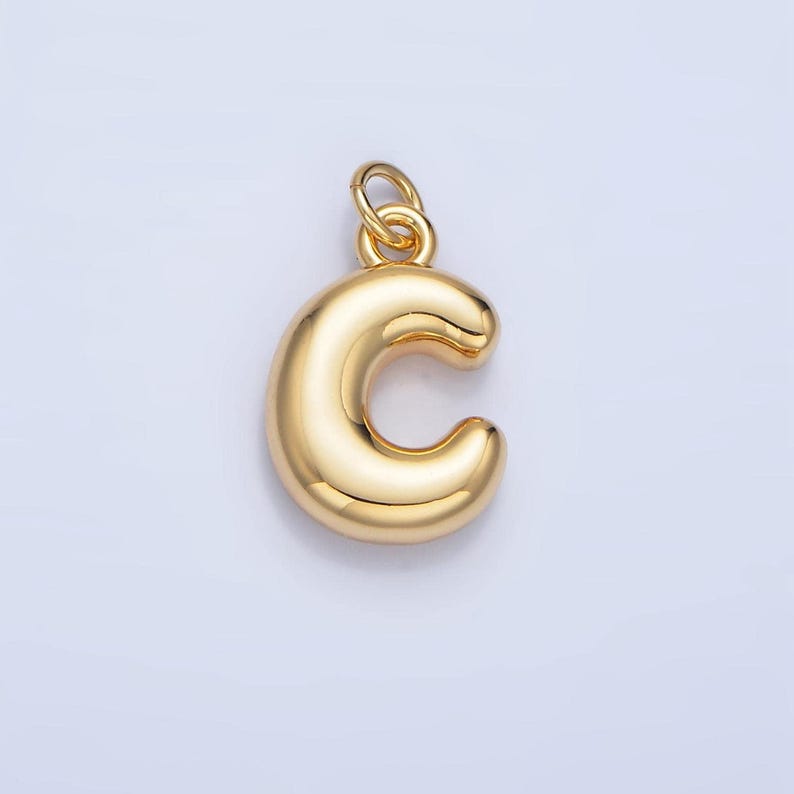 May include: A gold-colored charm in the shape of the letter C. The charm is smooth and has a shiny finish.