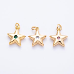 May include: Three gold star charms, each with a loop for hanging. The stars have a green, clear, and pink gemstone centre. The charms are displayed against a white background.