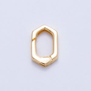 May include: A gold-colored, hexagonal clasp. The clasp is a solid, geometric shape with a hinged opening. The metal has a polished, reflective surface. The clasp is designed to connect two pieces together.