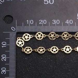 May include: Gold-colored chain featuring a repeating pattern of open circles with star cutouts. The chain is displayed against a black background with a ruler for scale. The chain's design is visible in detail.