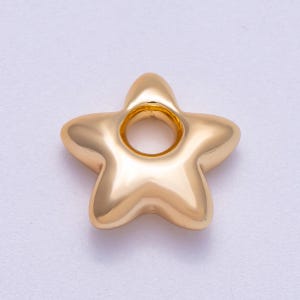 Puede incluir: Una cuenta dorada en forma de estrella con un agujero en el centro. La cuenta tiene una superficie lisa y pulida y bordes redondeados. Este componente de joyería es ideal para crear collares, pulseras y pendientes.
