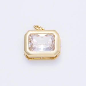 May include: A gold-colored pendant with a large, rectangular, clear gemstone. The gemstone is set within a gold frame, and the pendant has a small loop at the top for a chain. The design is simple and elegant.