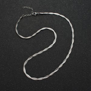 May include: A silver chain necklace with a twisted design. The chain is laying flat on a black surface.