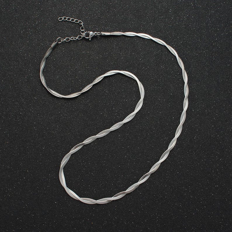 May include: A silver chain necklace with a twisted design. The chain is laying flat on a black surface.