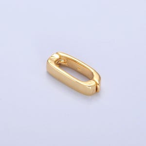 May include: A gold-colored, rectangular clasp with rounded edges. The clasp has a hinged design, allowing it to open and close. The metal has a polished finish, reflecting light. The clasp is designed for jewelry or accessories.