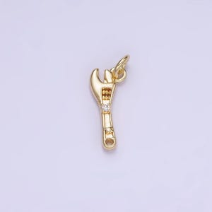 May include: A gold-toned wrench charm with a single clear rhinestone in the center. The charm has a loop at the top for attaching to a bracelet or necklace.