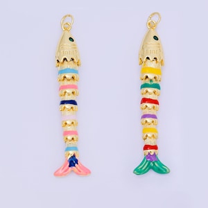 May include: Two gold-coloured fish pendants with colourful enamel details. One pendant features blue, pink, and navy accents, while the other has green, red, and purple. Both have a small green gem on the head and a loop for hanging.