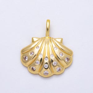 Peut inclure: Pendentif en forme de coquillage doré, avec une boucle pour une chaîne. Le pendentif est orné de petites pierres précieuses claires et roses. Le design en coquillage présente des nervures détaillées et une finition polie.