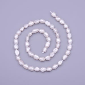 May include: A strand of white freshwater pearls, arranged in a circular pattern on a light purple background.