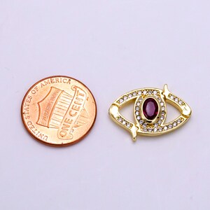 May include: Gold-tone eye charm with a red gemstone and clear rhinestones. The charm is about the size of a US penny.