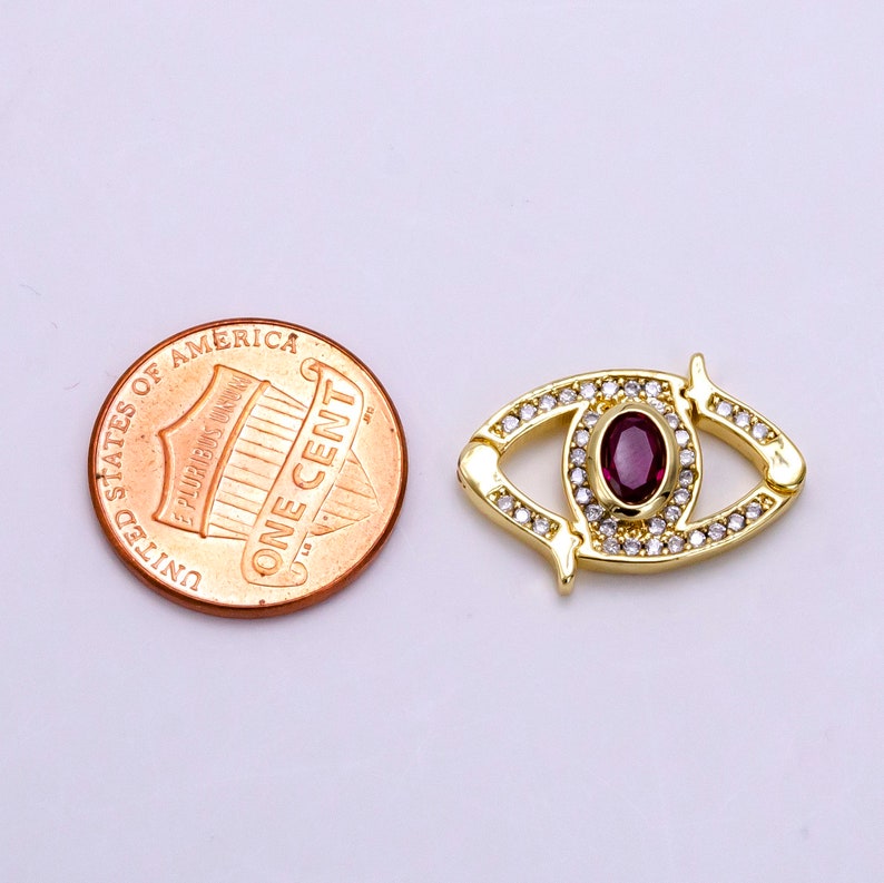 May include: Gold-tone eye charm with a red gemstone and clear rhinestones. The charm is about the size of a US penny.