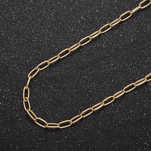 May include: A gold chain necklace with a simple oval link design. The chain is lying flat on a black textured surface.