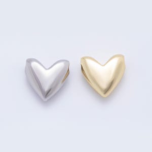 Könnte beinhalten: Zwei herzförmige Anhänger. Einer ist silberfarben und der andere goldfarben. Die Anhänger haben ein glattes, abgerundetes Aussehen und sind vor einem schlichten weißen Hintergrund platziert. Diese Anhänger könnten für die Schmuckherstellung oder andere Bastelprojekte verwendet werden.