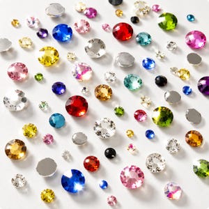 May include: A collection of round, faceted rhinestones in various sizes and colors, including red, blue, yellow, green, pink, clear, and black. These decorative gems feature a flat back and a multi-faceted top surface that reflects light.