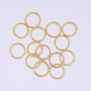 May include: A collection of gold-colored metal rings, scattered across a white surface. The rings are circular, with a consistent thickness, and appear to be made of a shiny, reflective material. The image is well-lit, highlighting the metallic sheen of the rings.
