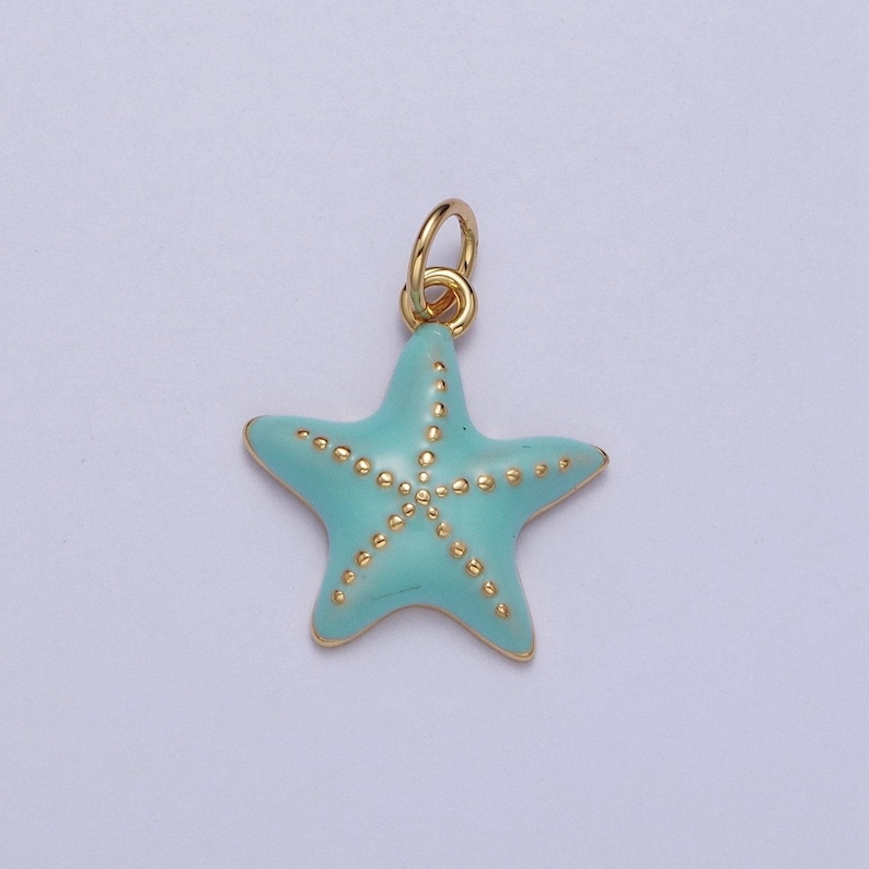 May include: A gold-colored starfish charm with a light blue enamel finish. The starfish has gold-colored dots and a gold-colored loop for attaching to a necklace or bracelet. The charm is a jewelry component.