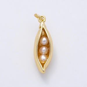 May include: A gold-toned metal pendant shaped like an open pea pod, featuring three small, round, iridescent white pearls nestled inside the pod. The pendant includes a small circular jump ring at the top for attachment to a chain or cord.