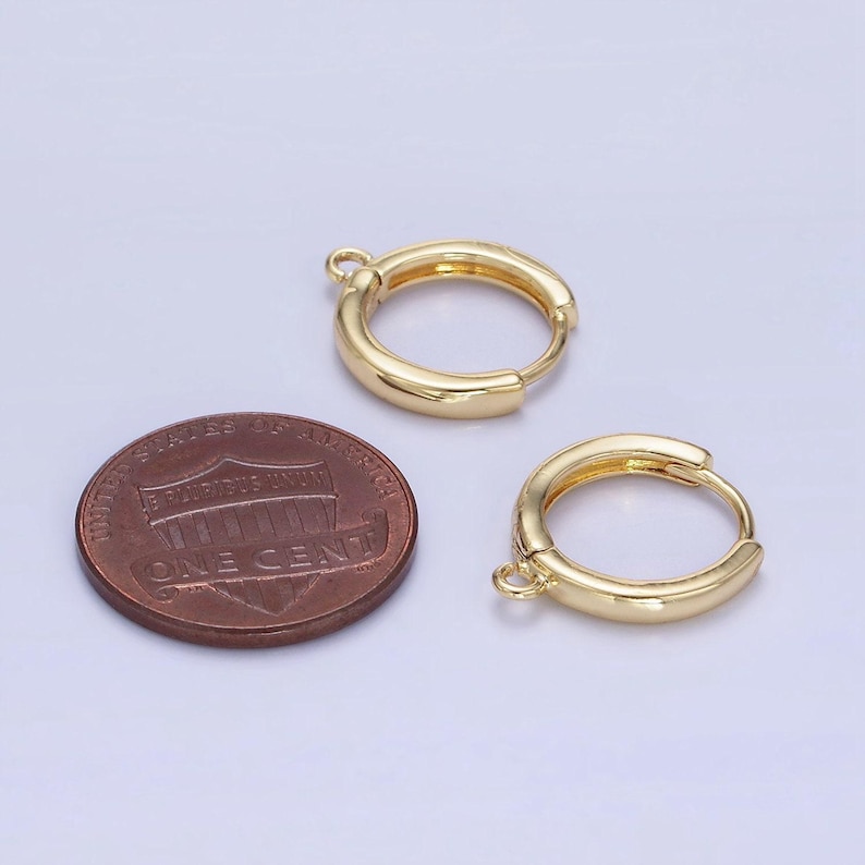 May include: Two gold-coloured hoop earrings with a small loop for attachment. A U.S. one-cent coin is next to the earrings for size comparison. The earrings have a smooth, polished finish and a simple, classic design.