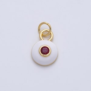 May include: A gold-colored pendant with a white enamel disc and a central red gemstone. The pendant has a small loop for attachment. The jewelry piece is likely a charm or a small pendant for a necklace or bracelet.