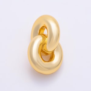 May include: A gold-toned pendant featuring two interlocking, smooth, rounded oval links. The metal surface has a polished, reflective finish, creating a continuous, connected loop structure that is uniform in color and texture throughout the piece.